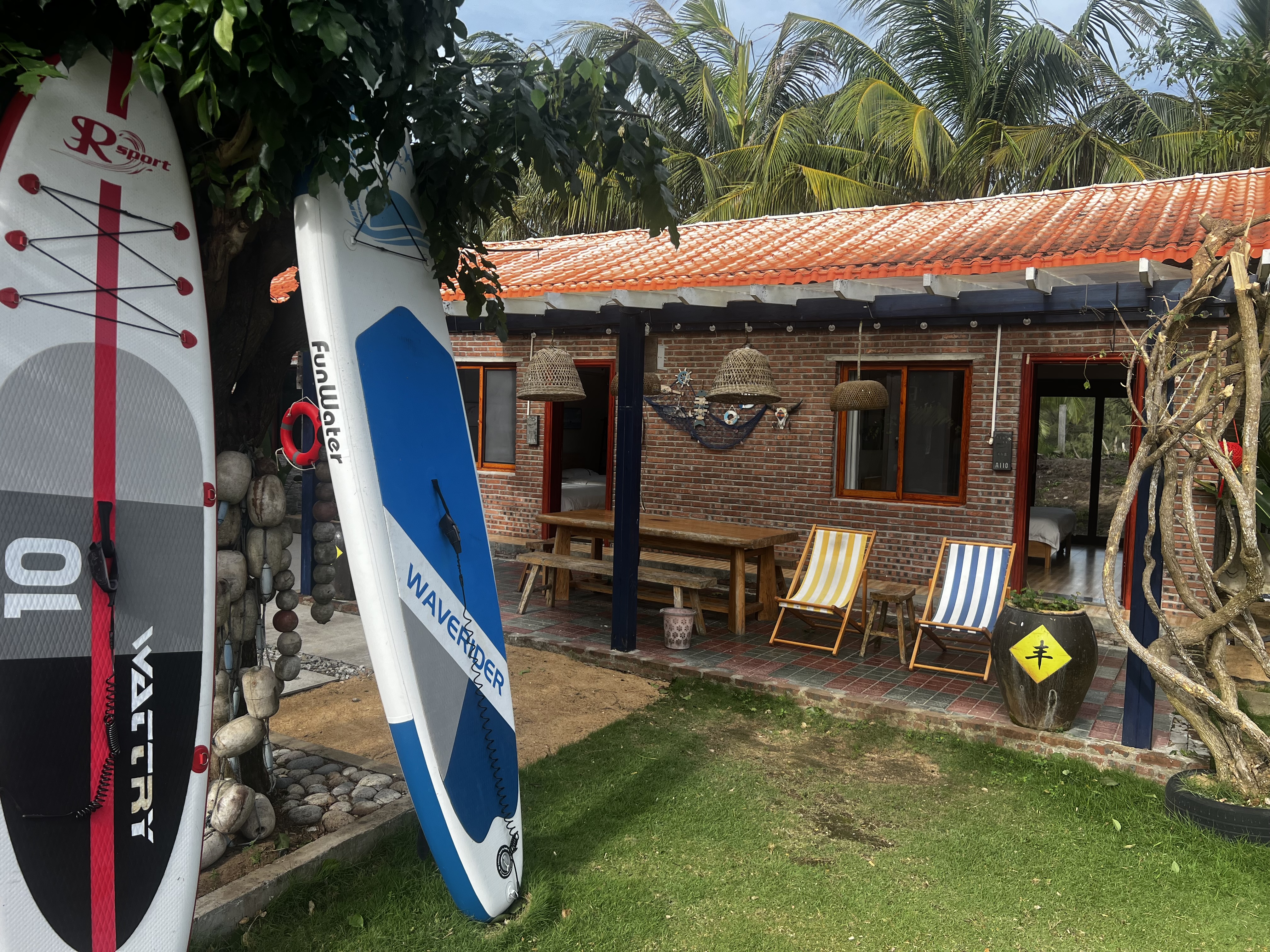 Surfboards and paddleboards in the garden with cottage in background