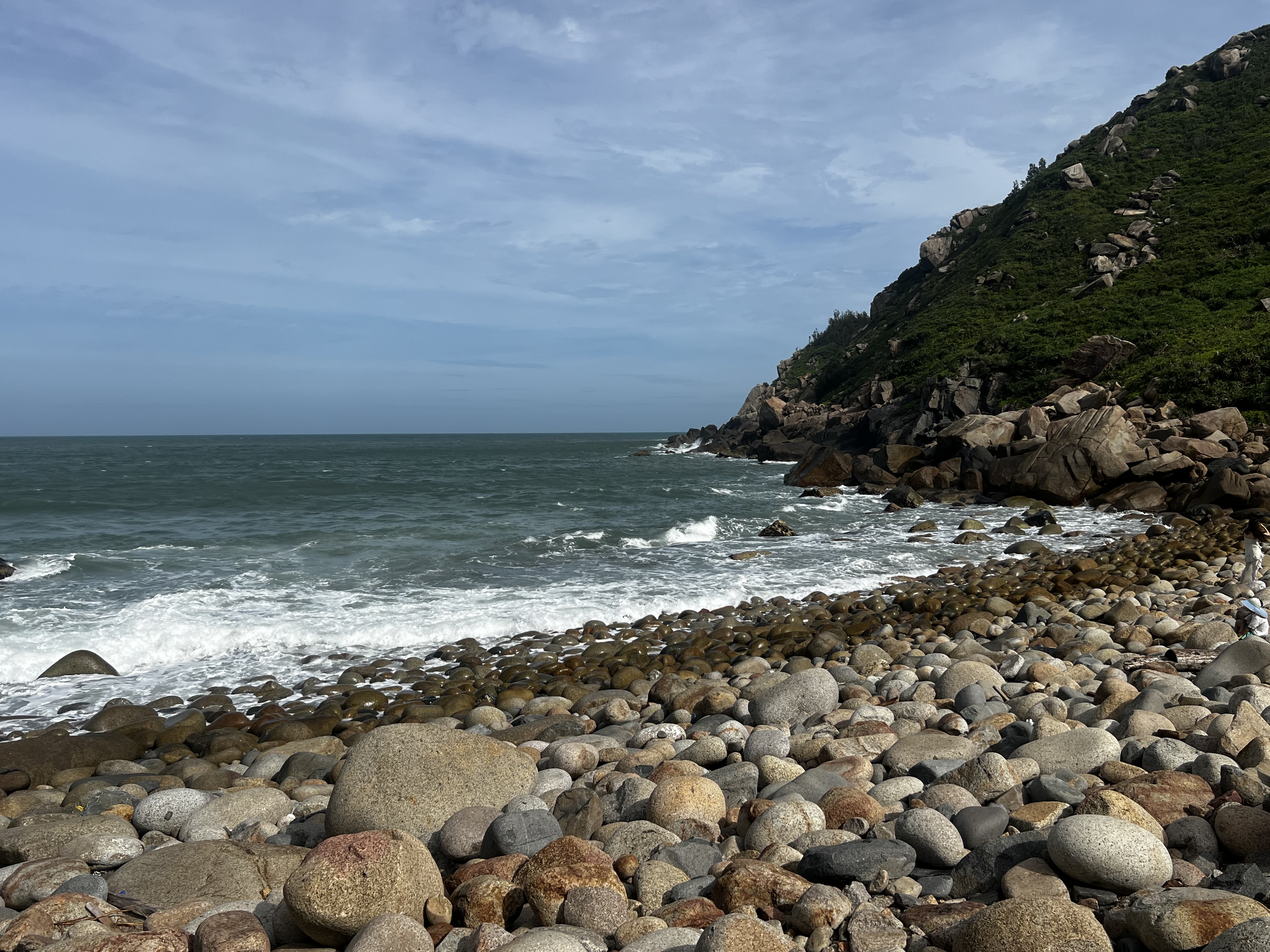 Rugged pebble beach with waves and green headland near Dahuajiao